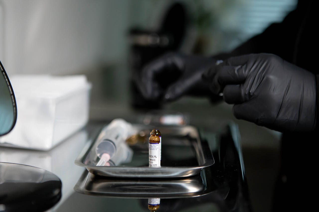 Close-up of gloved hands preparing a syringe with a vial on a metal tray in a clinical setting.