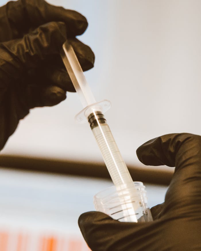 close-up-of-person-in-rubber-gloves-holding-a-tube-and-a-syringe-9259988 Close-up of a syringe handled with black gloves in a laboratory setting.