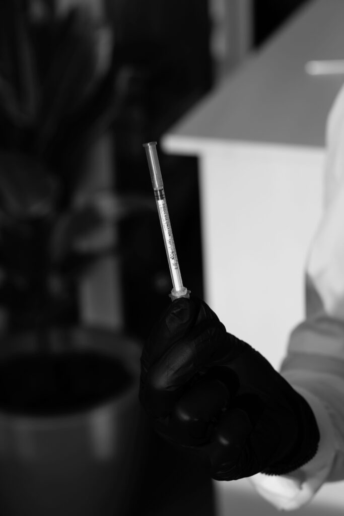Close-up black and white image of a syringe held by a gloved hand, emphasizing medical precision.
